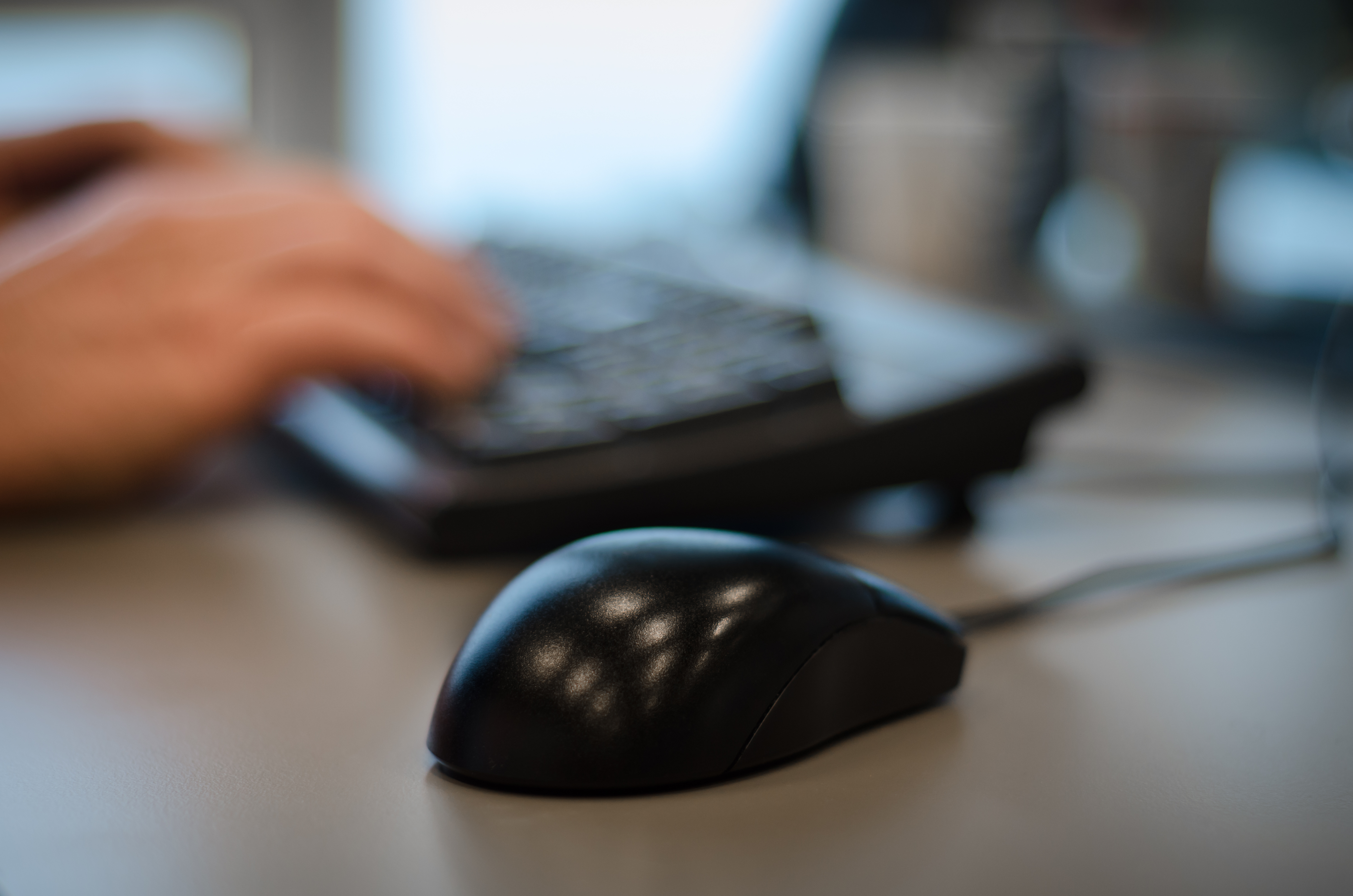 Black computer mouse and hands on a keyboard.