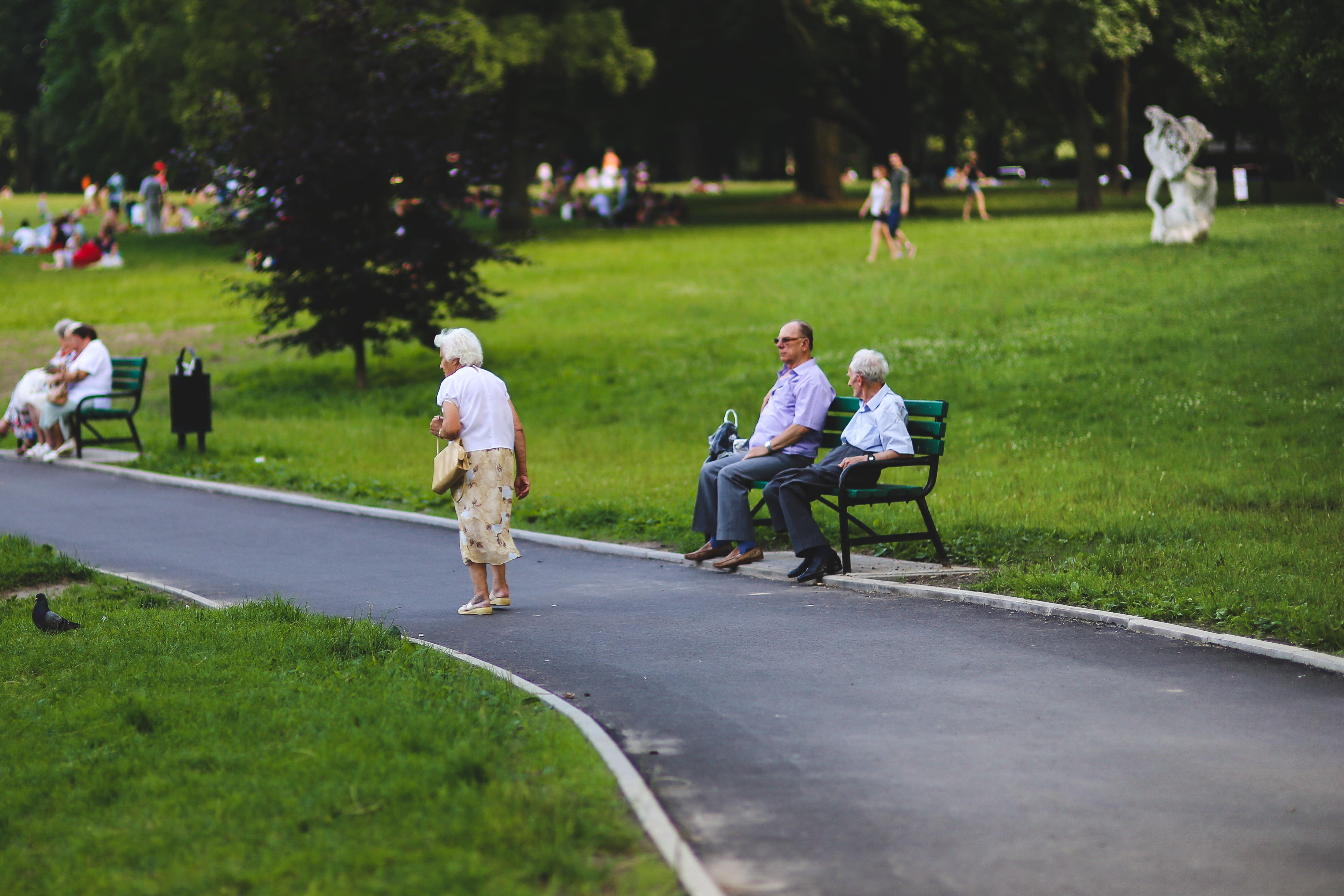 Seniors sitting on benches in a park and a woman walking in front of them.